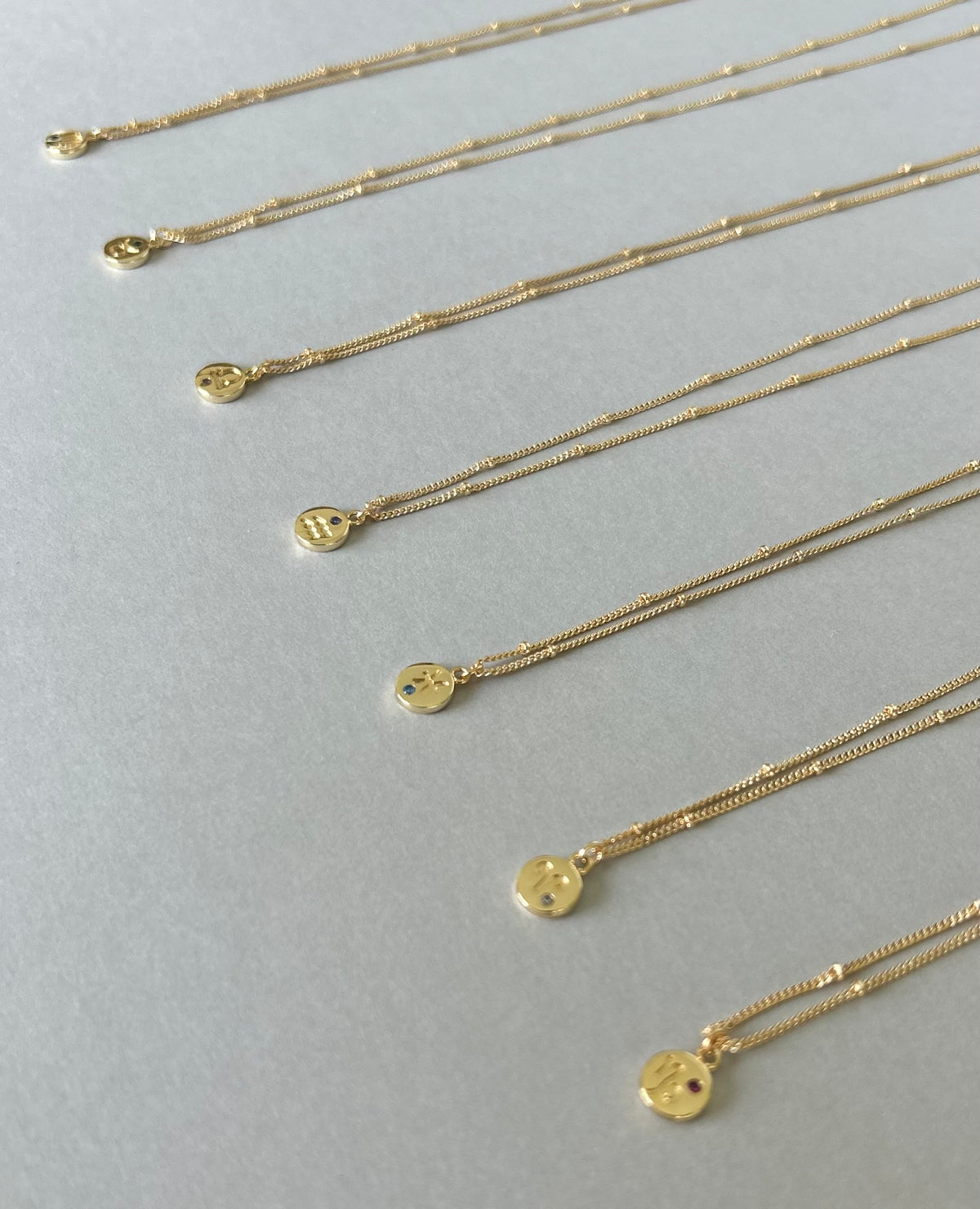 Gold plated Zodiac necklaces with fine bead detail chains on a pale background