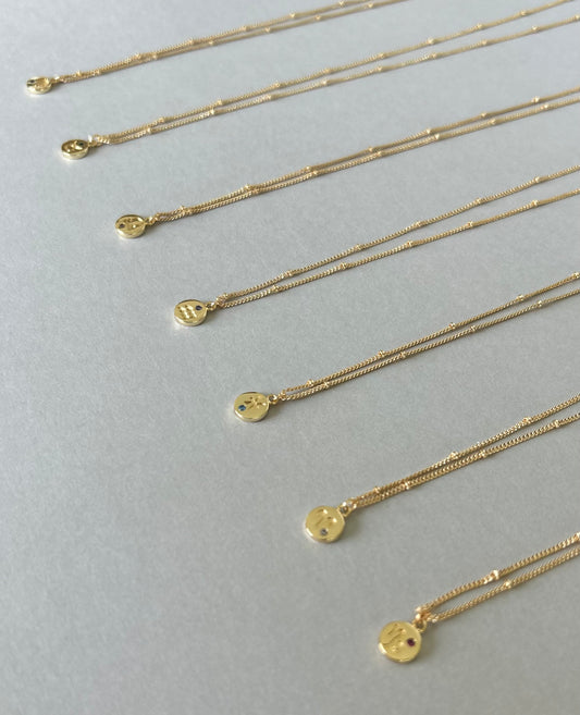 Gold plated Zodiac necklaces with fine bead detail chains on a pale background