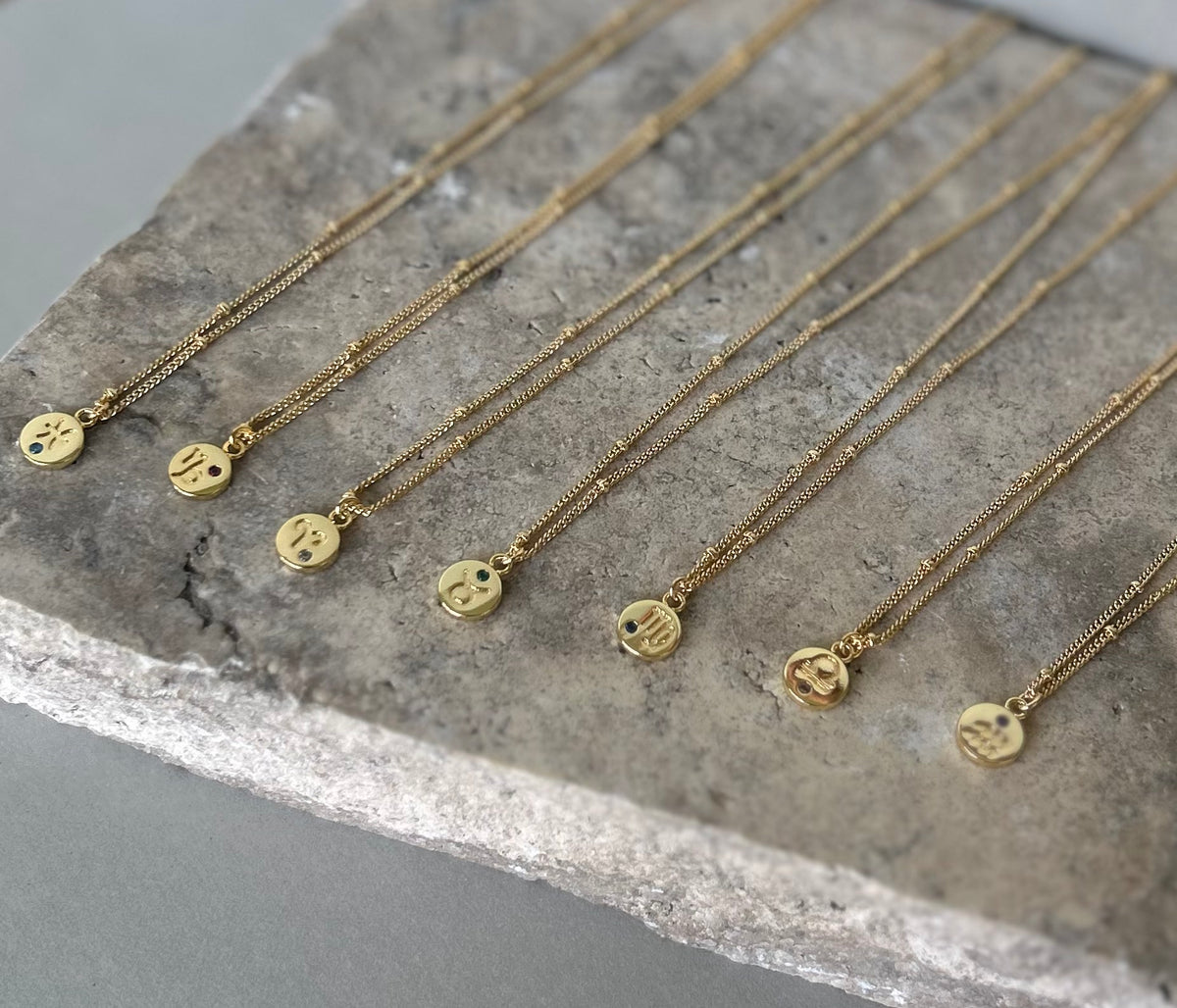 RUMI gold plated star sign pendant necklaces arranged on a stone display